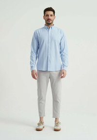 Chemise bleu clair à boutons, pantalon gris à rayures évasées et baskets crème, créant une tenue décontractée avec une coupe ample et des textures douces.