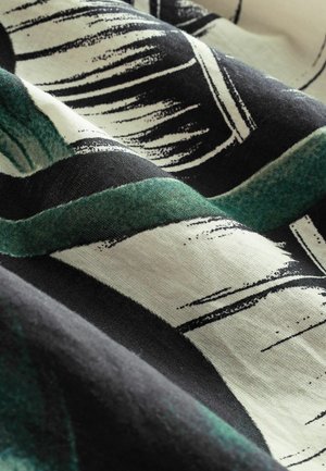 Katoenen stof in groen, zwart en crème. Heeft abstracte bladvormen met zichtbare textuur en zachte plooien die het ontwerp accentueren.