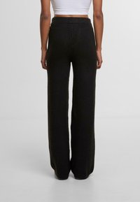 Černé úzké pletené kalhoty s širokými nohavicemi a texturovaným povrchem, s elastickým pasem pro pohodlí. Zobrazeno ze zadní strany na světlém pozadí.