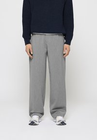 Pantaloni largi gri cu o textură fină, asortați cu un pulover tricotat bleumarin. Mai jos, adidași albi cu accente gri și bleumarin.
