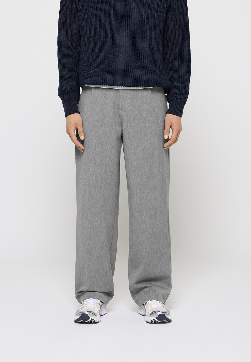Pantaloni largi gri cu o textură fină, asortați cu un pulover tricotat bleumarin. Mai jos, adidași albi cu accente gri și bleumarin.