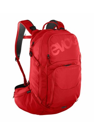 Sac à dos rouge en tissu durable, doté de bretelles rembourrées, de plusieurs compartiments et d'une poche latérale zippée pour le rangement.
