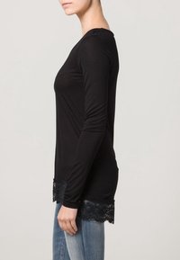 Camisa negra de manga larga con dobladillo de encaje, corte ajustado, cuello redondo y textura suave. Combinada con jeans azules.