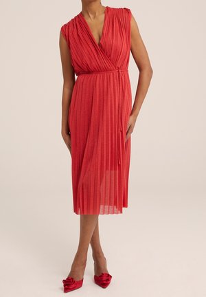 Robe portefeuille plissée rouge à manches courtes et taille nouée. Le tissu est léger et fluide, complété par des chaussures à talons hauts rouges assorties.