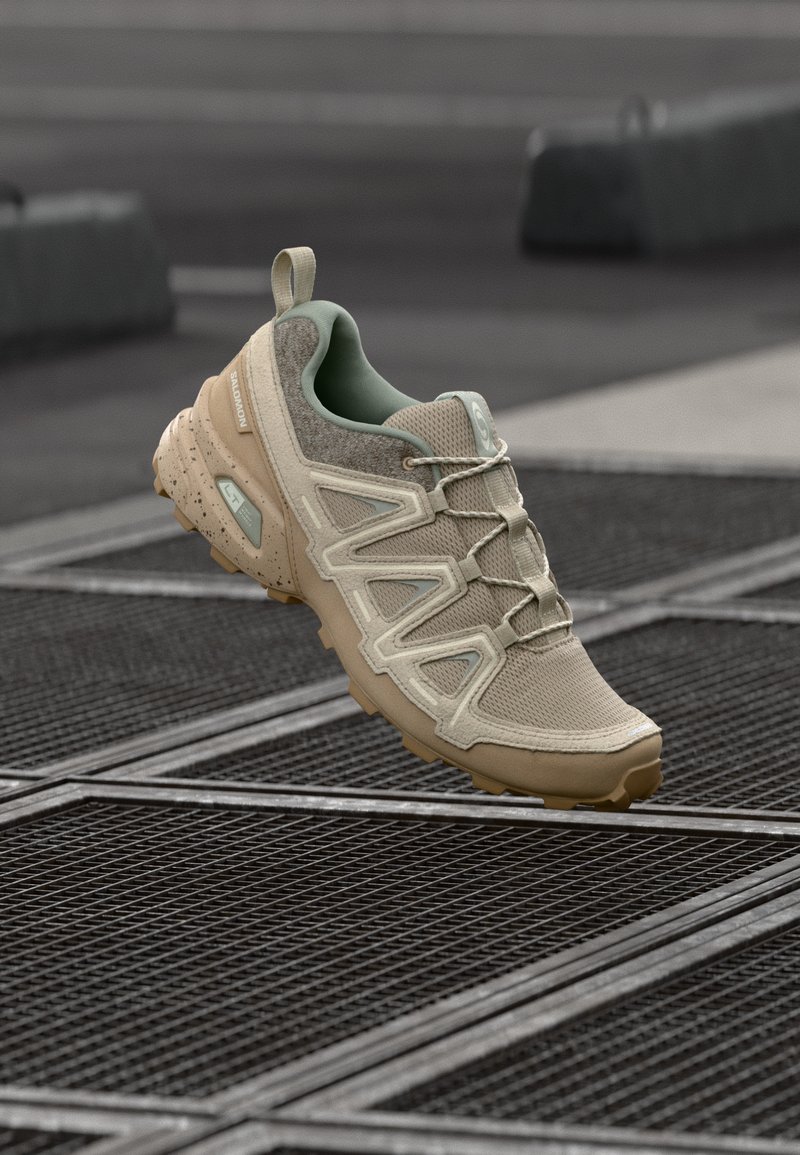 Sapatilha atlética bege com parte superior em malha texturizada, detalhes verdes e sola flexível. Design em zigzag notável e biqueira reforçada.