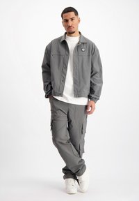 Grijze, knoopsluiting jas met een logo en elastische manchetten, gecombineerd met bijpassende cargobroek met zijzakken en een rechte pasvorm.