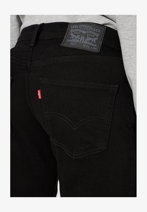 Schwarze Denim-Jeans mit einem Levi Strauss-Label, die eine Gesäßtasche mit einem markanten geschwungenen Stickmuster und einem kleinen roten Etikett aufweist.