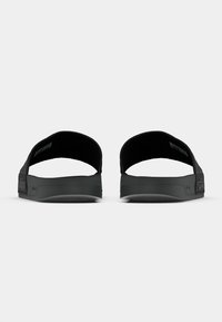 Melnas slidenu sandales ar teksturētu siksnu un mīkstinātu zolīti. Tās ir ar izteiktu logotipu sānos un atvērtu aizmuguri.