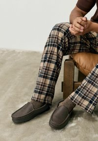 Bruine leren instappers, tan- en marineblauwe geguite broek met een duidelijke patroon, textuur van gebreide bruine sokken, zittend op een houten stoel.