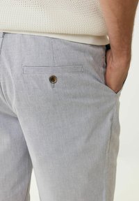 Leichte gestreifte Hosen mit einem Knopfverschluss, seitlichen Taschen und einer glatten Stofftextur. Die Streifen sind in Blau- und Weißtönen.