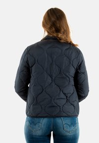 Giubbotto trapuntato blu scuro in tessuto a shell, con un motivo a onde unico. Il design include un colletto semplice ed è leggero.