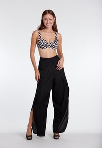 Black wide-leg pants with front slits, paired with a black and white geometric patterned bikini top. Smooth fabric and open design.