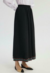 Fustă maxi neagră cu talie elastică, având broderie florală în roșu și verde pe margine. Material neted și croială lejeră.