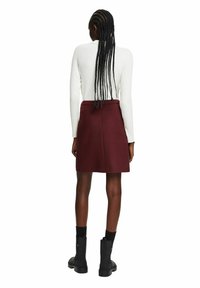 Jupe bordeaux à texture lisse, avec une taille ajustée et une coupe évasée, associée à un pull blanc côtelé et des bottines noires.