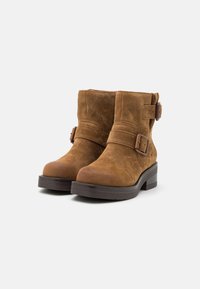 Brown suede ankle boots with dual buckles, textured surface, rounded toe, and a thick, sturdy brown sole.