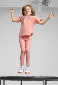 T-shirt in cotone rosa con grafica "PUMA" e leggings rosa. Grafica di personaggi sui leggings. Sneakers bianche e rosa con dettagli a fiocco.