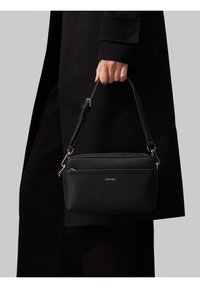 Sort læderhåndtaske med lynlås i toppen, justerbar rem og sølvfarvet hardware. Har en forlommer og glat tekstur.