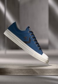 Blue sneaker with a smooth synthetic upper, white rubber sole, and a prominent black star logo. Features black laces and a textured toe cap.