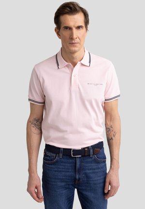 Lyserød polo skjorte med kontrasterende sorte striber på kraven og ærmerne, lavet af blødt stof. Bæres med mørkeblå jeans og et vævet bælte.