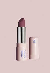 Korres True Velvety Lipstick vaaleassa vaaleanpunaisessa putkessa, sylinterimäisessä muodossa. Huulipunan väri on hillitty luumu, ja sen pinta on matta.