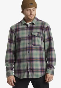 Groene en paarse geruite flanellen overhemd met een borstzak, zwarte knopen en een zachte, gestructureerde stof; gedragen over een licht shirt.