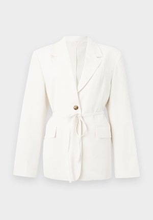 Blazer blanc cintré avec revers crantés, un bouton marron, ceinture à nouer à la taille, et poches à rabat de chaque côté.