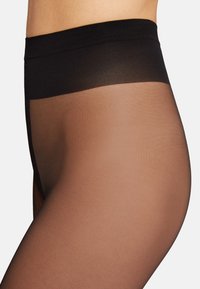 Tights trasparenti color nude con una ampia vita nera. Il materiale è liscio, presentando una transizione graduale da opaco nella parte superiore a trasparente in basso.