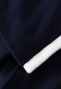 Marineblaue Fleece-Stoff mit weichem weißem Besatz. Verfügt über eine glatte Textur und sichtbare Nähte, die Wärme und Komfort betonen.
