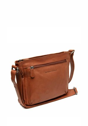 Bolso cruzado de piel marrón con un bolsillo frontal con cremallera, correa ajustable y textura suave. Presenta un logotipo de la marca grabado en el costado.