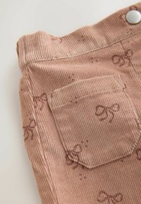 Tessuto di velluto a coste rosa con un sottile motivo a fiocco, caratterizzato da una tasca posteriore e un bottone argentato, superficie a costine texturizzata.