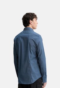 Camicia a maniche lunghe con motivo blu, collo a punta, polsini con bottoni e orlo leggermente curvo, caratterizzata da un tessuto con trama tattile.