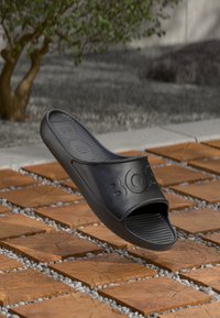 Crni gumeni klompa s teksturiranom unutrašnjošću i "BOSS" ugraviranim na gornjem dijelu. Dizajn s otvorenim prstima i glatkim, zakrivljenim rubovima.