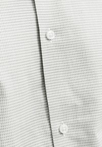 Gros plan d'une chemise blanche avec un motif quadrillé texturé et deux boutons blancs fixés le long de la patte de boutonnage.