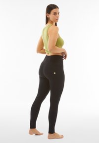 Leggings neri a vita alta con una trama liscia e dettagli di cucitura sottili, abbinati a un crop top aderente a coste di un verde chiaro.