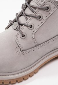 Botte imperméable grise en suède lisse, avec des lacets ronds, des œillets hexagonaux et une semelle extérieure en caoutchouc à adhérence texturée.