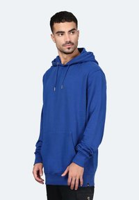 Felpa blu con vestibilità rilassata, coulisse, tasca frontale e polsini a coste. realizzata in materiale morbido, con una texture liscia.
