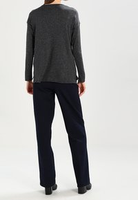 Graues Langarmoberteil mit lockerer Passform; kombiniert mit marineblauen Hosen. Glatter Stoff, dezente seitliche Schlitze und abgerundeter Saum.