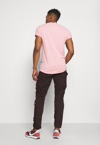 Cămașă scurtă, roz deschis, combinată cu pantaloni cargo închisi. Adidași cu accente roșii. Design simplu, material din bumbac și croi lejer.