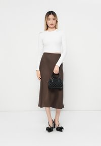 Bijela uska bluza s dugim rukavima, smeđa satin midi suknja, crna torba s teksturom s dva ručka i crne cipele s visokom potpeticom ukrašene mašnicama.