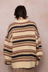 Pletený sveter v krémovej farbe so pruhovanými vzormi v tmavo hnedých, červených a béžových odtieňoch. Má rebrovaný golier a voľný strih. Detailné textúrované priadze.