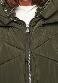 Chaqueta acolchada en verde oliva con diseño acolchado, cierre de cremallera en la parte superior y capucha ajustable. Fabricada en un tejido ligero y brillante.