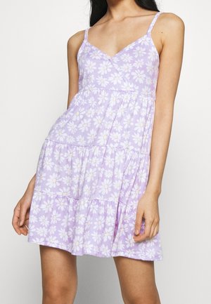 Fioletowa sukienka na ramiączkach z dekoltem w kształcie litery V, cienkimi ramiączkami, kwiatowym wzorem białych stokrotek, rozkloszowaną spódnicą z falbanami oraz miękkim, lekkim materiałem.