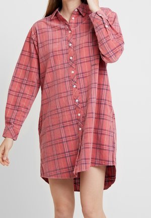 Punainen ja sininen ruudullinen pitkähihaista mekkoa, jossa nappi edessä, kaulus, sivureiät ja hieman kaareva helma. Tyylitelty käännetyillä hihoilla.