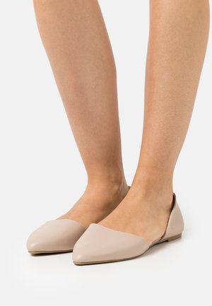 Beżowe płaskie buty ze spiczastym noskiem, wykonane z gładkiej skóry. Posiadają niski obcas i odkryty tył, co ułatwia zakładanie.