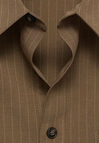 Col et boutons de chemise à fines rayures marron, tissu légèrement texturé avec des rayures verticales fines, premier bouton défait.