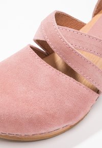 Rosa Wildlederschuh mit Querverriegelungen, abgerundeter Zehenpartie und einer Holzsohle mit sichtbaren Nähdetails. Glatte Oberfläche.