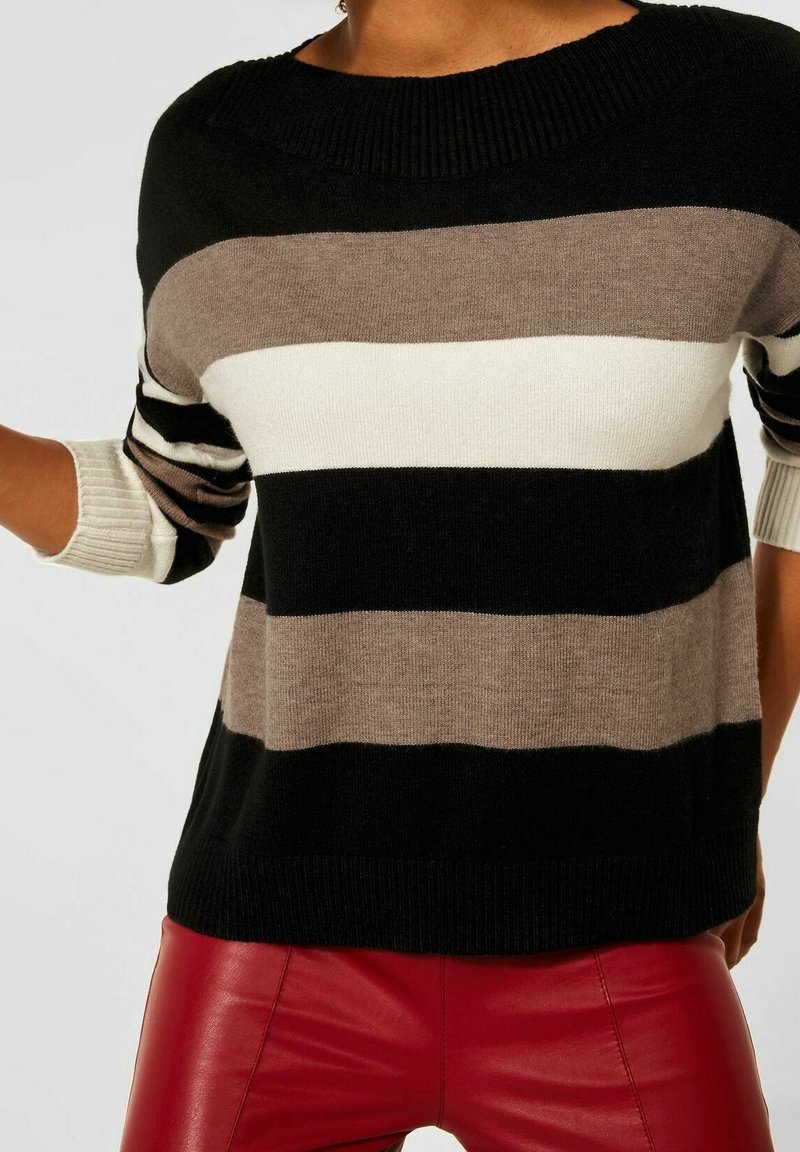 Svart, brun och krämrandig tröja med vid halsringning och ribbade ärmslut. Bärs med röda läderbyxor, vilket framhäver kontrasten i texturer.