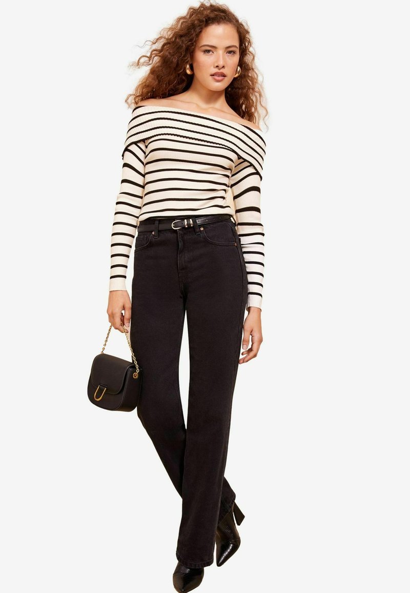 Top a spalle scoperte crema e nera a righe abbinato a jeans neri a vita alta. Gli accessori includono una piccola borsa nera e tacchi.