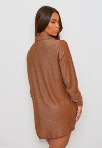 Vestido camisero de mangas largas de color marrón con brillo metálico, con cuello, corte relajado y una textura suave, que presenta un diseño de longitud a mitad de muslo.