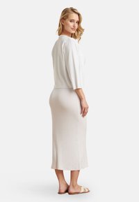 Lichtgrijze, geribbelde trui met driekwart mouwen, gecombineerd met een bijpassende lange, aansluitende rok. De outfit is eenvoudig en strak.